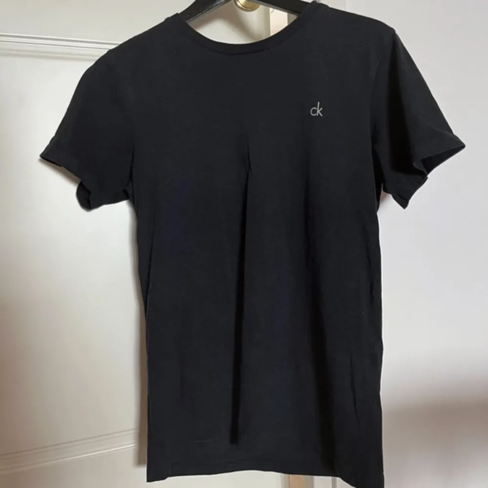 Svart Calvin Klein t-shirt med diskret tryck. Bredd axlar 42 cm. Bredd under ärmarna 46 cm. Längd 65 cm. OBS‼️ storlek 164/176 men använd som XS. T-shirts.