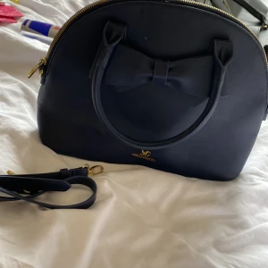 Holly&Whyte väska - En blå Holly&Whyte väska med guld detaljer och dekorativ rosett. Tillkommer en axelbandsrem.