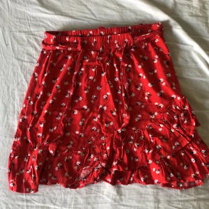 Röd Blommig Kjol från Lindex - Jättebra skick, nästan aldrig använd! Fina volanger och bara jättenajs till sommarn! Storlek S men det finns såna här band att dra så man kan anpassa💞 Köpren betalar frakt🩷