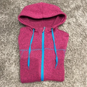 Fleecejacka med luva - Zip Hoosiers i fleece i cerise med turkosblå detaljer. Fin kvalitet. Sparsamt använd.