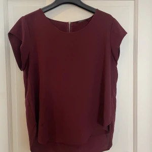 Blus - Tunn blus i vinröd färg, har en dragkedja i nacken som slutar 1 dm längre ner. I mycket gott skick 