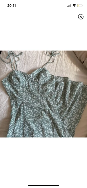 Grönblommig långklänning - Grön långklänning med hög slits och vita blommor. Smock i ryggen, knytband och markerade kupor. Knappt använd. 