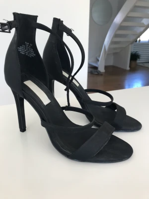 Svarta sandaletter stl 37/38 satin Nya - Högklackade festskor från H&M consious collection. Svart satin. Klackhöjd 10 cm. Stl 37, men stora i storleken, passar mig som är en 38:a. superfina på med rem runt vristen. Aldrig använda. Nypris 799:-