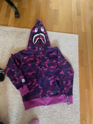 Bape Hoodie - Säljer Bape Hoodie som sonen ej använder. Strl L. Är som en small/ medium. Ca strl 170 cl. Färg: rosa/lila/ blå Bra bomullskvalitet. Bra dragkedja.   Är knappt använd.  Se bilder. Finns för upphämtning i Sollentuna / Rotebro Alt. Fraktas  