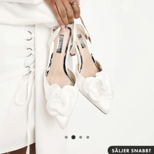 Klackskor - Vita klackskor med en medelhög klack. Jättefina och sköna klackskor med en vit blomma. Endast använda en gång, då de var lite för stora för mig. 