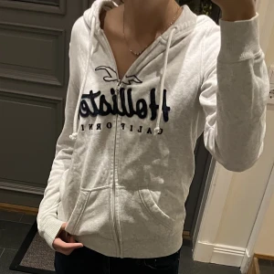 Ljusgrå hoodie med dragkedja från Hollister - Grå kofta från Hollister i storlek XS, skulle dock säga att den passar mer som S. Fint skick. Jag är 170 och brukar ha S i tröjor och den passar bra för mig. Använd gärna köp nu! Jag säljer även jeansen!