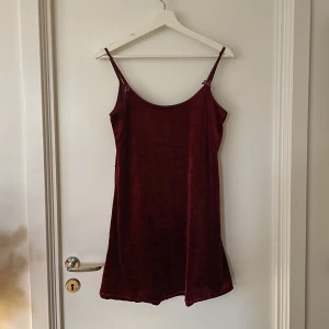 Vinröd slip in sammetsklänning - Vinröd sammetsklänning som slutar strax ovanför knäna. Har två små rosetter som detalj vid axelbanden