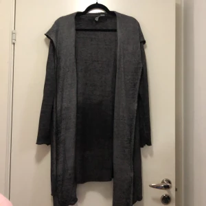 Asymmetrisk kofta - En gråspräcklig asymmetrisk kofta i bomull & polyester. Fickor samt luva. Använt men fint skick.