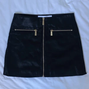 Ivyrevel ”läderkjol” - Svart läderliknande kjol i polyester med gulddetaljer från Ivyrevel. Jättefint skick! Knappt använd. 