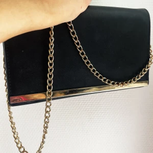 Axelremsväska  - En fin axelremsväska att ha  på fest eller utgång. Svart med guld kedja. Har lite repor på guldiga kanten (se bild).
