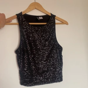 Svart topp med paljetter - Svart topp/linne med svarta paljetter på framsidan, kortare modell perfekt till fest