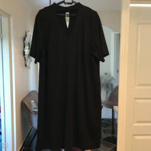 Klänning - Svart klänning med urringning framtill och polodetalj vid halsen. 