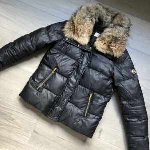 Svart jacka Michael kors strl S - Svart dunjacka från Michael Kors med avtagbar pälskrage och gulddetaljer. Fint skick, endast ett hål i ena fickan som ej syns. Strl S