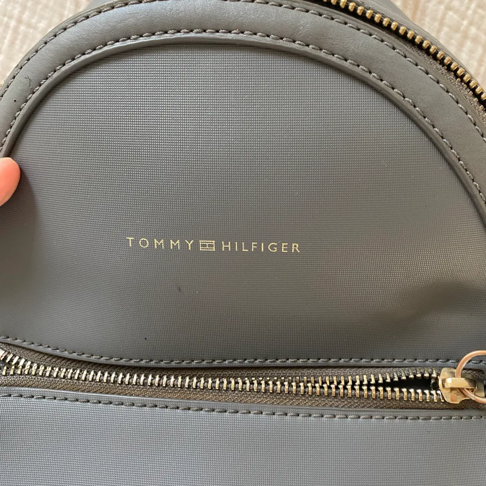 Sjukt snygg grå Tommy Hilfiger mini ryggsäck. Ca 30x20x15cm. Mindre slitage på dragkedjan därav bra pris . Väskor.