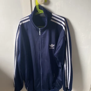 Adidas tränings jacka - Mörk blå. Condition 6,5/10 lite borr här och där men andå användbar. Dragkedjan fastnar ibland men den kan ändå dras upp. Står inte strl men skulle säga S/M 