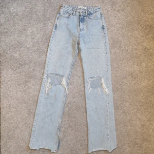 Jeans blå - Supersnygga straight-jeans med hål vid knäna och slits vid slutet av benet. Helt oanvända i storlek 32.