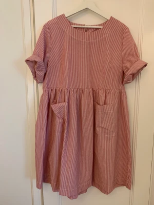 Randig bomullsklänning - Vit- och rödrandig klänning i 50% bomull/50% polyester. Fint skick, inget att anmärka på. Strl M-XL, beroende på passform.   Hämtas vid Nobeltorget eller postas mot frakt på 70 kr.