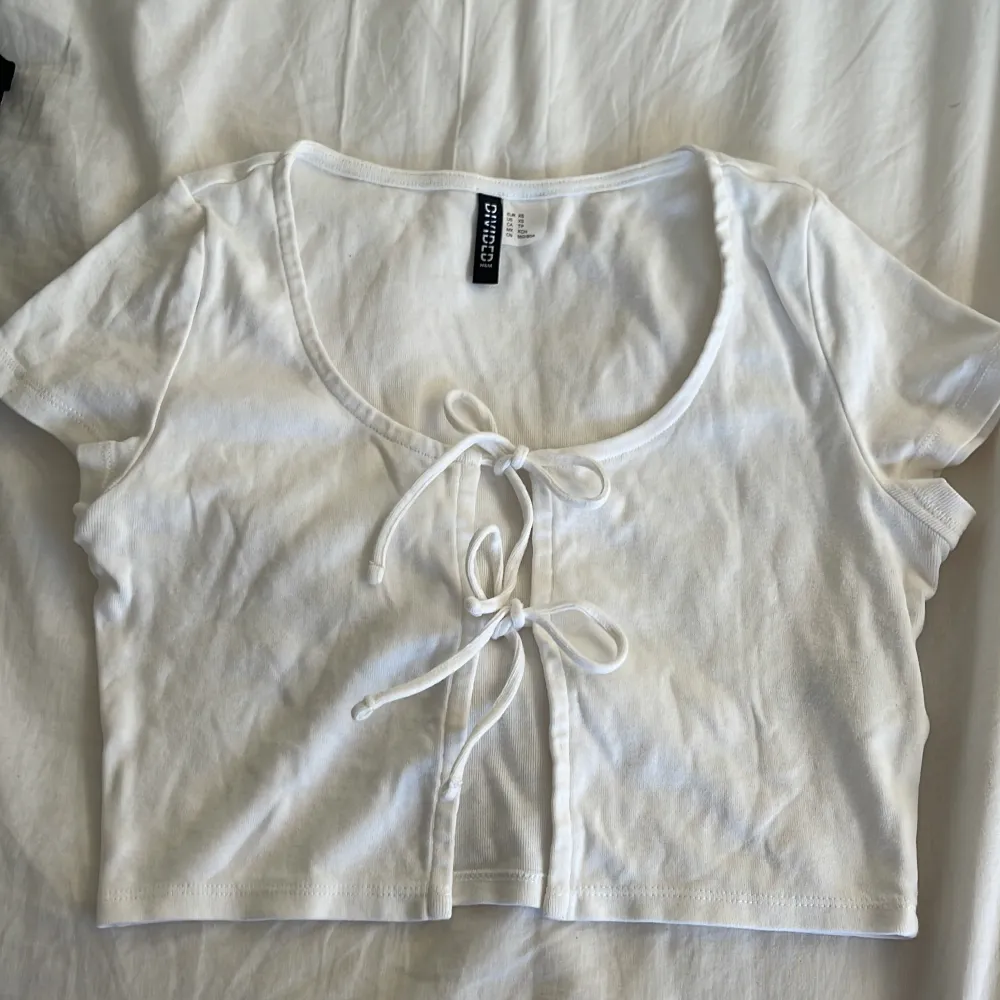 Ett vitt klädesplagg som kan användas som tröja o kofta, med 2 rosetter man kan knyta . Toppar.
