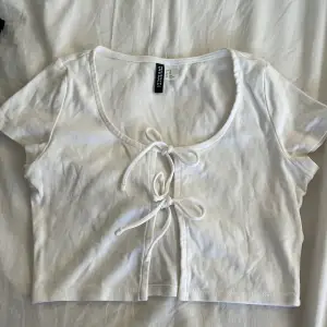 Ett vitt klädesplagg som kan användas som tröja o kofta, med 2 rosetter man kan knyta 