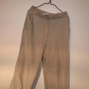 Beiga raka kostymbyxor - Beiga kostymbyxor med slits ifrån hm, rak modell och nästan aldrig använda . Väldigt skrynkliga på denna bild men går ju självklart att stryka