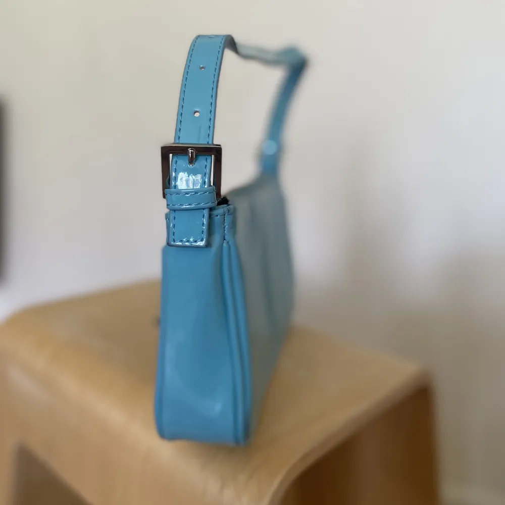 Blå handväska i lackmaterial från Gina Tricot. Använd ett fåtal gånger, men i gott skick. Mindre fläck på ena sidan som är ett fabriksfel.. Väskor.