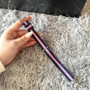 Daniel Wellington klockarmband - Säljer ett klassiskt Daniel Wellington armband i rosa och blå, med guldiga detaljer. Sparsamt använd, fint skick.