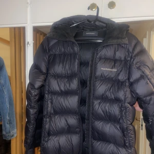 Vinterjacka peaprefomance dun - Jätte varm och fluffig vinterjacka, har inte frusit en dag i denna snygga jacka. Jackan har en fodrad luva, fickor med dragkedja samt liftkorts ficka på ena armen. Jackan är snygg, svart och trendig. Nypris 4100kr, använd 2 vintrar💖