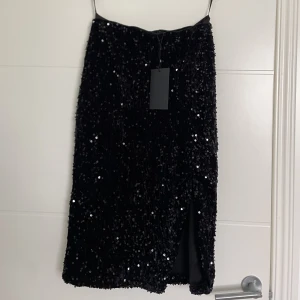 Svart kjol, glittrig - Glittrig svart kjol med slits, aldrig använd och lappen sitter kvar💃🏽💃🏽 Man kan ha den både lågmäldas och högmidjad, lågmidjad så når den precis under knäna.  Storlek xs men passar s också