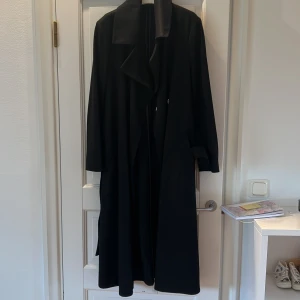 Kappa - Svart kappa med omlottknäppnig samt skärp. Ok på baksidan. Perfekt skick, nästan oanvänd 