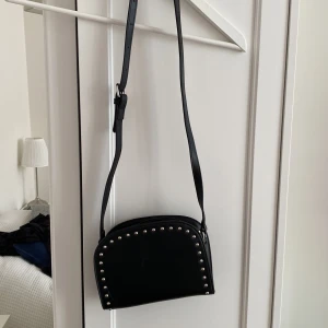 Axelremsväska - Pieces - Svart axelremsväska med ”nitar” från Pieces. Den har ett stort ”huvudfack” samt en lite ficka på baksidan. Liten skråma på framsidan, därav det billiga priset. Säljer då den inte kommer till användning💕✨
