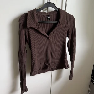 Brun långärmad tröja - Säljer denna fina långärmade tröja, den har en krage med knappar så man kan justera hur lång urringning man vill ha. I stolen M men liten så skulle säga S men passar Xs också. Skriv gärna vid frågor eller vid fler bilder🩷