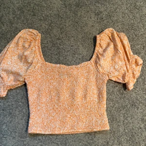 Söt topp med blommönster  - Super söt topp i orange och vitt blomönster med puffärmar. Verkligen så fin!