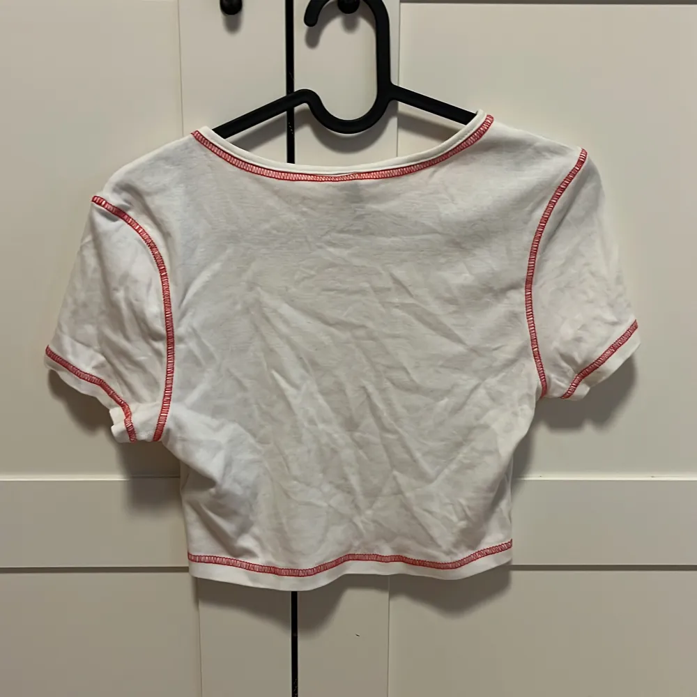 Bekväm, stretchig, en liten fläck så liten som en fläck, monterad./ fitted crop top, stretchy, comfortable. A stain as tiny as a small speck.  White with red outlines and figure of the sun. . Toppar.