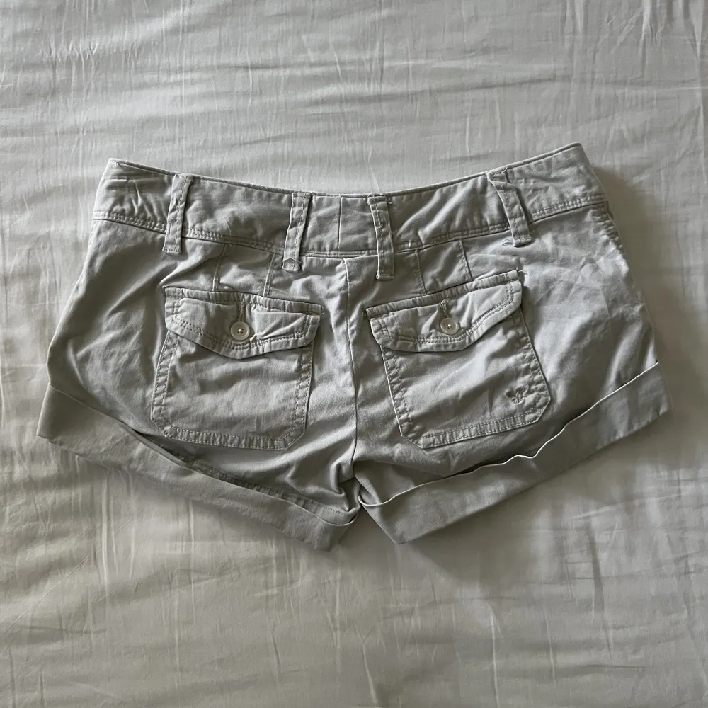 Supersöta vintage beige-gråa lågmidjade mini shorts med unika bakfickor. Begagnat skick, men inga fläckar eller hål! Midjemått mätt rakt över: 37cm, längd: 20cm. Storlek 34🫶💕. Shorts.