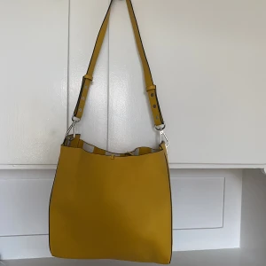 Gul väska från zara - Gul mellanstor väska från zara, den går att vända ut och in och har randig. Har en tillhörande necessär i. Sparsamt använd, fint skick.