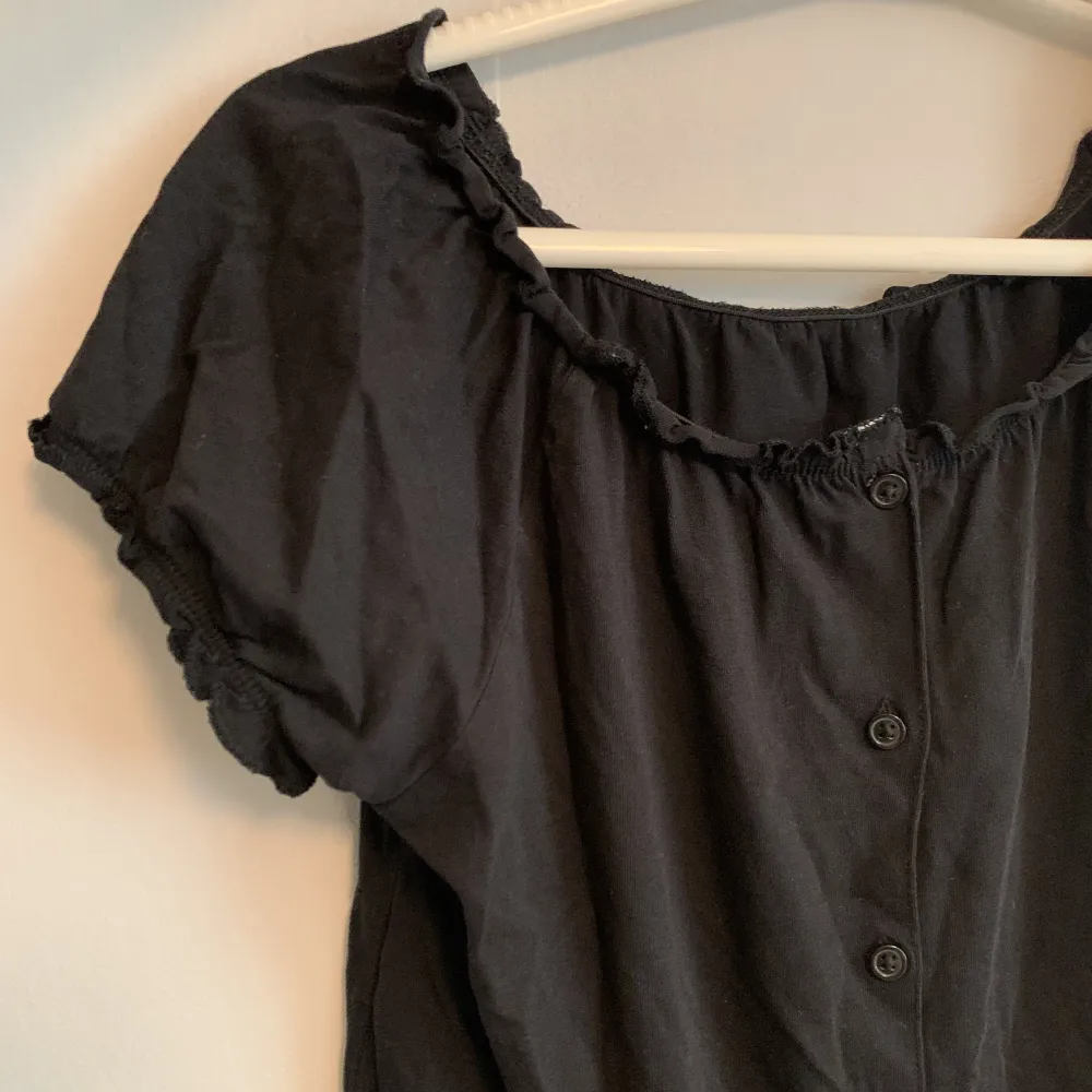 Gullig svart topp med knappar och elastisk krage, kan bäras som off shoulder 🖤. Toppar.