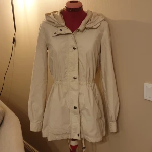 Klassisk parkas - Beige vindjacka från Vero Moda. Borttagbar luva och reglerbar i midjan. 
