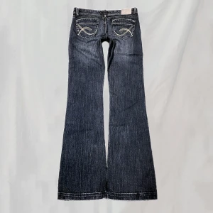 Jeans - Midja:82 innerben:87 Jeans med guldfärgat broderi. Stora på mig, svårt att visa passform. Mörkblå med lite skiftning i grön/brunt. Något nötta vid fickor, linning, gren,fotändar. Vid fickorna kan dock va design då de har samma placering.Överlag bra skick🤍