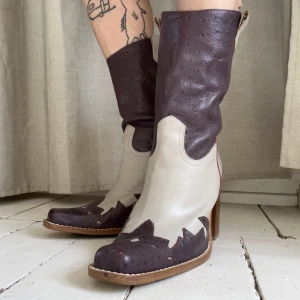 Cowboyboots skinn - Lila och beiga cowboyboots med röda detaljer, lagom hög klack i trä, bekväma att gå i. Nästintill oanvända i jättebra skick, dock finns liiiite skav på ena tån (bild 3).