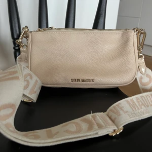 Steve Madden väska  - Axelbandsväska från märket Steve Madden. Beige med gulddetaljer. Inköpt för 1299kr för 1/2 år sedan och använd ett fåtal gånger. 