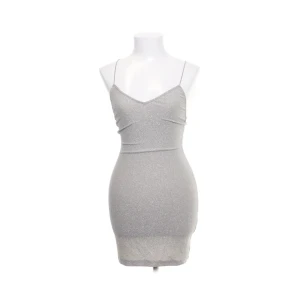 Silverglittrig bodycon  - Kort ärmlös glittrig klänning med elastiska smala axelband, korsade i ryggen och djup v-ringning. Aldrig använd, lapp kvar.   Hund finns i hemmet och köpare står för frakt.