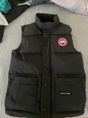 CANADA GOOSE Freestyle väst (Svart) - Hej! Säljer nu min svarta goose väst, original och köpt för nypris för ca 5.000kr på Johnells (kolla nupris på johnells).  Den är i bra skick då jag tar hand om mina plagg, inte använd så många gånger trots åren pga Sveriges väder. Kan gå ner i pris.