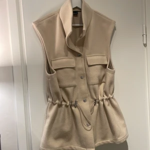 Väst Maja Nilsson lindelöf x Ginatricot  - Beige väst med justerbara resårband i midjan. Använd fåtal gånger 