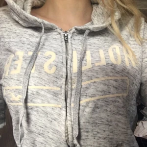 Grå Hollister hoddie - Säljer nu min gråa hollister hoddie då jag inte andvänder den längre. Inga synliga skador förutom lite missfärgad text. (KLICKA INTE PÅ KÖP NU)