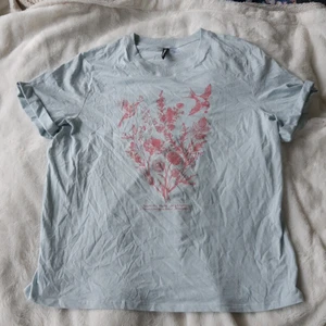 Ljusblå T-shirt från HM - Aldrig använd t-shirt från HM Divided med rosa fågel- och växtmotiv🌺