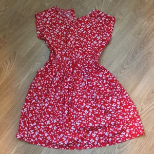 Klänning  - En röd blommig klänning som har knapp för att stängas i nacken  2 fickor på sidorna 