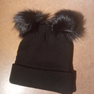 Svart mössa  - En helt ny mössa med så söta bollar på huvudet som liknar snapshat-öron 😻 Ribbstickad och bra med stretch, så den passar de allra flesta huvuden. Endast testad, helt ny. Säljer för 50 kr 🖤
