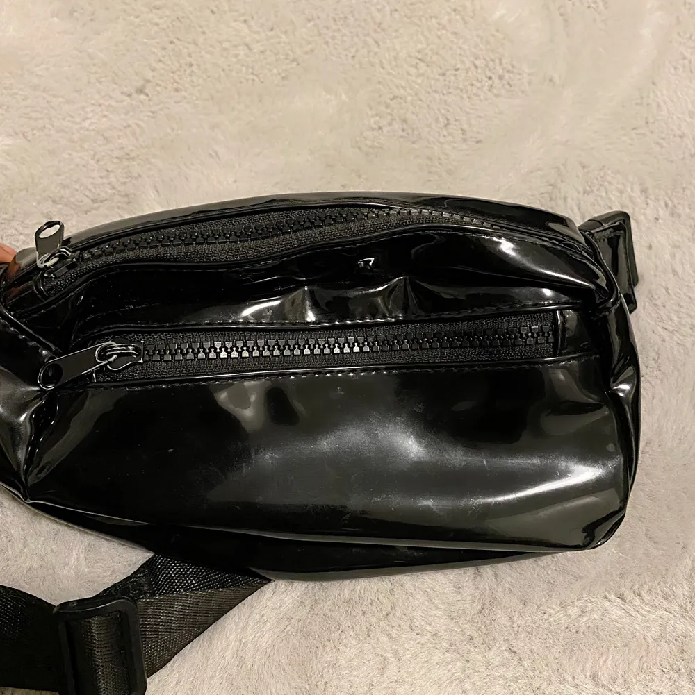 En svart magväska med dragkedjor uppe och nere med ett bälte som du kan spänna åt. . Väskor.