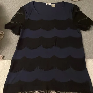Topp med spets  - Fin och mjuk secondhand kortärmad topp med svarta spetsdetaljer framsidan och i armar i rak passform,rund halsringning. Gjorda i 80 % modal 20% bomull 100% polyester. Finskick. Längd  ca. 60 cm i stl 36/38