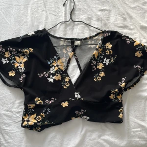 Urringad blus - Urringad blommig blus i en kortare modell med öppen rygg. (Fråga om du vill se en bild med plagget på)